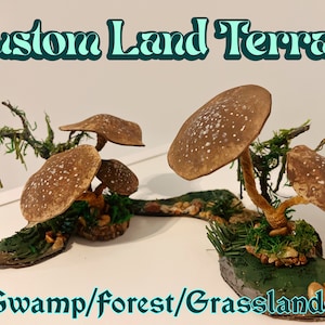 Puede incluir: Dos escenas de terreno personalizadas en miniatura que presentan estructuras con forma de hongo con tapas marrones y blancas moteadas. Las escenas están ambientadas en una base verde con rocas y vegetación. El texto "Swamp/Forest/Grasslands" se muestra debajo de las escenas.