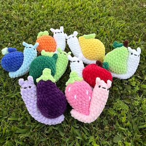 May include: A collection of handmade crochet snails in various colors and fruit-inspired designs. The snails feature a variety of colors, including blue, orange, green, yellow, red, pink, and purple. Each snail has a unique fruit-themed shell, such as a strawberry or lemon.