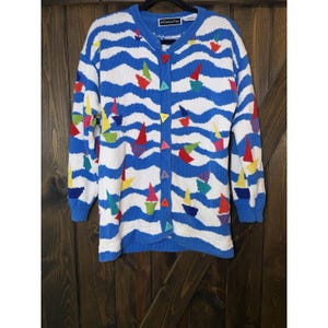 May include: A long-sleeve knit cardigan featuring a blue and white wavy pattern with small colorful sailboat motifs throughout. The garment has a crew neckline and a front button closure with triangular buttons in various solid colors.