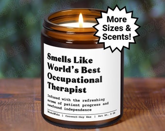 May include: A brown glass candle with a white label that reads "Smells Like World's Best Occupational Therapist". The label also includes the text "Infused with the refreshing aroma of patient progress and newfound independence". The candle is on a wooden surface. A yellow starburst with the text "More Sizes & Scents!" is in the upper right corner of the image.