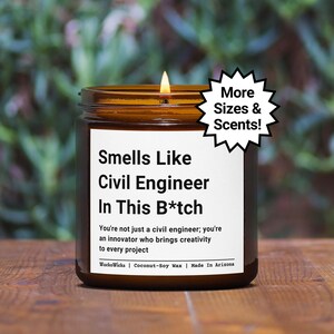 May include: A brown glass candle with a white label that reads "Smells Like Civil Engineer In This B*tch". The label also includes the text "You're not just a civil engineer; you're an innovator who brings creativity to every project." and "WackoWicks | Coconut-Soy Wax | Made In Arizona". A yellow flame is burning at the top of the candle.