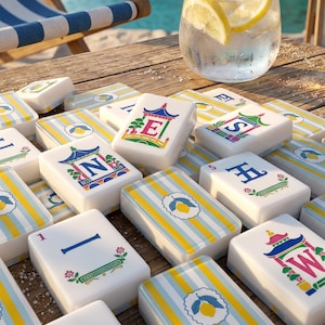 May include: A set of mahjong tiles featuring white and yellow striped backs with lemon icons, and faces displaying letters E, N, S, W, and numerical symbols with pagoda illustrations. A glass of water with lemon slices sits nearby.