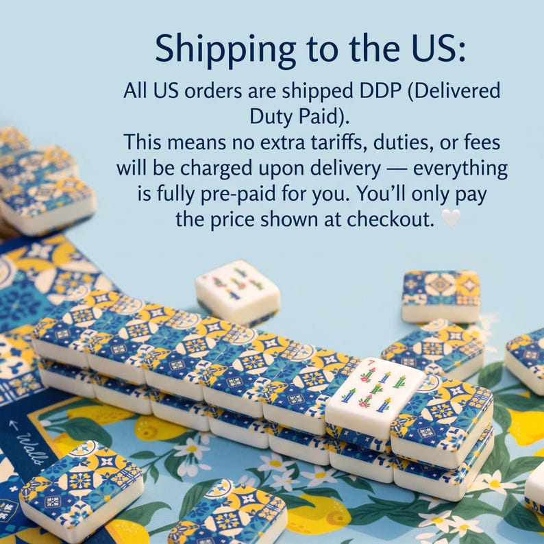 May include: A set of mahjong tiles featuring a blue, yellow, and white geometric tile pattern on the back. The front of one tile displays a green bamboo design with the number seven. The tiles are arranged on a surface with a lemon and floral print.