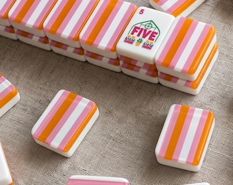 Puede incluir: Una colección de fichas de mahjong rectangulares con un patrón de rayas verticales repetitivas en naranja, rosa y blanco. Una ficha muestra un gráfico de invernadero verde con la palabra FIVE y el número 5 impresos en rojo encima.