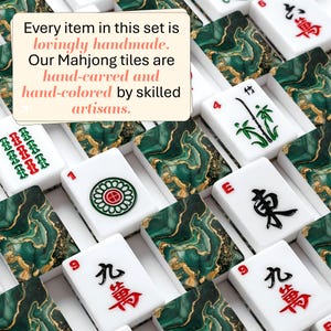 May include: A collection of Mahjong tiles featuring a white base with green and gold marbled patterns on the back. The front faces display black, red, and green engraved symbols, numbers, and characters. A text overlay reads: Every item in this set is lovingly handmade. Our Mahjong tiles are hand-carved and hand-colored by skilled artisans.