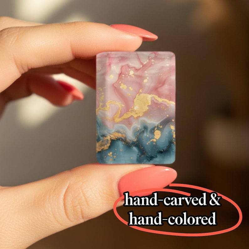 May include: A rectangular piece featuring a marbled pattern in shades of dusty pink, deep teal, and white, accented with gold flecks. The text hand-carved & hand-colored is visible at the bottom. This item has a smooth, polished surface finish.