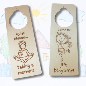 May include: Two wooden door hangers with a cutout for a doorknob. The left hanger has a drawing of a person meditating with the text "Quiet please... Taking a moment". The right hanger has a drawing of a person dancing with the text "Come In! It's Playtime!"