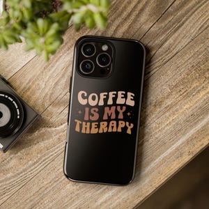 May include: Black phone case with a white and brown graphic that says "Coffee is my therapy".
