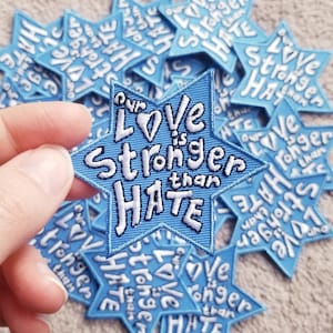 May include: A blue star-shaped patch with white embroidery that reads "Our Love is Stronger than Hate".