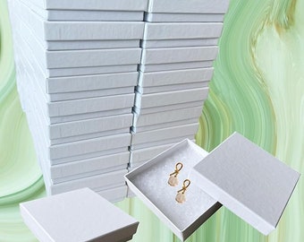 May include: A stack of 20 white cardboard boxes with a single box open and two gold earrings inside. The earrings are on a white background.