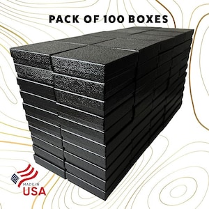 May include: A stack of 100 black cardboard boxes. The boxes are stacked neatly and are all the same size. The text "PACK OF 100 BOXES" is printed on the top of the stack. A "MADE IN USA" label is visible at the bottom of the image.
