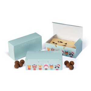 May include: Three light blue gift boxes with white polka dots. One box is open, revealing a light-colored treat. The boxes are decorated with cartoon animals and the text "MERRY CHRISTMAS". Several chocolate truffles are scattered around the boxes.