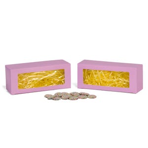 May include: Two rectangular, light purple gift boxes with clear window cutouts, filled with yellow shredded paper. A small pile of round cookies with colorful sprinkles sits in front of the boxes. The boxes are on a white background.