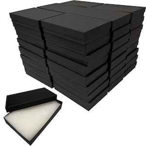 May include: A stack of black gift boxes, with a lid and a separate base. One box is open, revealing white padding inside. The boxes are rectangular and appear to be made of cardboard or a similar material. The boxes are suitable for jewelry or small gifts.