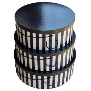 May include: A set of three stacked round storage boxes with a glossy black lid and a black and white vertical striped pattern on the sides. Each box features a thin black rope handle attached to the side for carrying or lifting the lid.