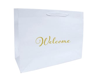 Könnte beinhalten: Eine weiße Geschenktüte mit Henkel und dem Wort "Welcome" in goldener Schrift. Die Tasche ist rechteckig und scheint aus Papier oder einem ähnlichen Material zu bestehen. Der Hintergrund ist schlicht weiß.
