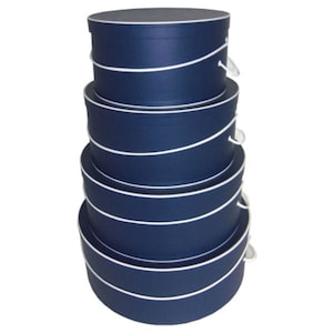 May include: Set of four round hat boxes in navy blue with white trim and rope handles. The boxes are stacked on top of each other, with the largest box at the bottom and the smallest box at the top.