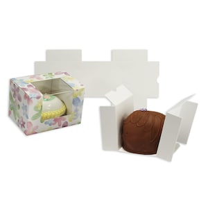 Può includere: Due scatole, una assemblata e una piatta, progettate per prodotti da forno. La scatola assemblata presenta un motivo floreale e una finestra trasparente, che mostra una piccola torta. L'altra scatola è bianca e contiene una leccornia ricoperta di cioccolato.