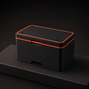 May include: A rectangular storage box with a matte black finish and a vibrant orange trim accenting the lid. The container features a hinged lid design with a central latch mechanism on the front and four small rectangular cutouts on the top surface.