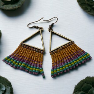 May include: A pair of triangle-shaped earrings with a fringe of colorful beads. The beads are in shades of orange, green, and purple.