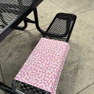 May include: A black metal picnic table with a pink and white floral patterned fabric covering the bench seat.