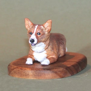 Puede incluir: Una figurita de cerámica pintada a mano de un perro corgi marrón y blanco acostado sobre una base de madera.