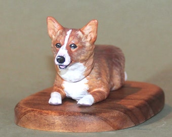 Puede incluir: Una figurita de cerámica pintada a mano de un perro corgi marrón y blanco acostado sobre una base de madera.