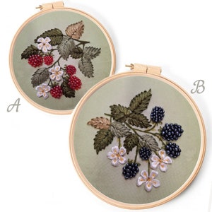 May include: Two embroidery hoops with different colored berry designs. The hoop labeled 'A' has a green and gold branch with red berries and white flowers. The hoop labeled 'B' has a green branch with black berries and white flowers.