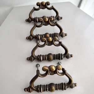 May include: Four antique brass drawer pulls with ornate scrollwork and a warm, aged finish. Each pull features a curved handle and decorative center detail, perfect for adding vintage charm to furniture.