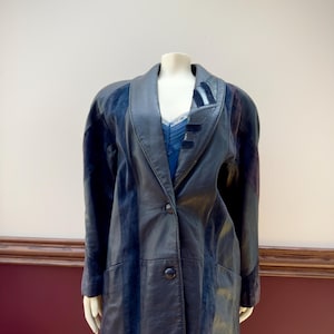May include: A vintage black leather jacket with a notched collar and button fastening. The jacket features dark blue suede panels on the front and sleeves. The jacket is displayed on a mannequin.