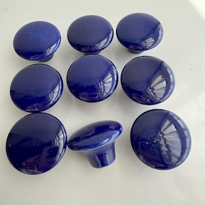 Peut inclure: Neuf boutons de placard en céramique bleu marine. Les boutons sont ronds avec une finition brillante. Un bouton est tourné sur le côté, montrant la tige. Ces boutons conviennent à la restauration de meubles ou aux projets de bricolage.