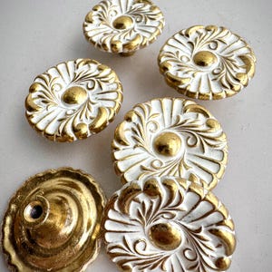 Peut inclure: Ensemble de six boutons de meuble décoratifs blancs et dorés. Les boutons présentent un motif floral avec des détails dorés et un bouton central doré. L'un des boutons comprend une plaque de montage dorée.