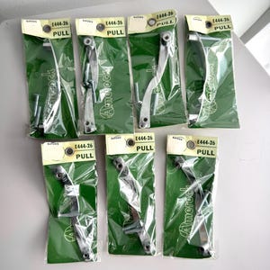 May include: Seven packets of Amerock E444-26 pulls are shown. Each silver-toned pull is in a clear plastic bag with a green backing. The packaging includes the word "PULL" and the brand name. Ideal for cabinet or drawer hardware.