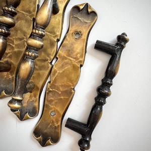 May include: A set of antique brass door handles and backplates. The handles have an ornate design with a dark brown finish. The backplates are a lighter brass colour with a textured surface. The hardware is likely for a vintage door.