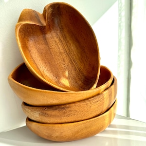 May include: Four wooden bowls stacked on top of each other. The bowls are heart-shaped and made of a light brown wood.