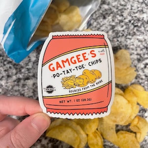 May include: A pink and white sticker with the text "GAMGEE'S est 3020" and "PO-TAY-TOE" CHIPS. The sticker also says "NON GMO" and "SOURCED FROM THE SHIRE" and "NET WT. 1 OZ (28.3G)".