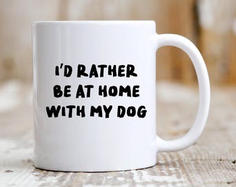 May include: White ceramic coffee mug with black text that reads "I'd rather be at home with my dog".