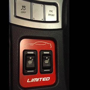 May include: A close-up of a car's interior console featuring buttons and switches. The image shows buttons for "OFF", "VSC SPORT", and heated seats. The red panel reads "LIMITED" with a car silhouette.