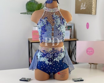 May include: A blue and white dance costume with a halter top, a skirt, and shorts. The costume is decorated with rhinestones and flowers. The costume is on a mannequin.