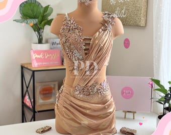 May include: A gold dance costume with a jeweled bodice and skirt. The costume has a draped skirt and a jeweled neckline. The costume is on a mannequin.