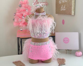 May include: Pink dance costume with a sparkly crop top and shorts, adorned with feathers and rhinestones. The costume includes matching arm warmers.