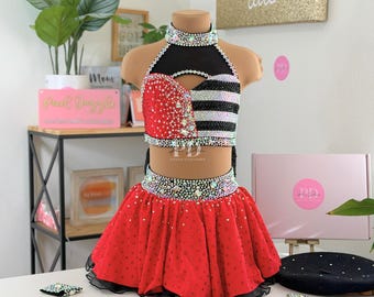 May include: A dance costume with a red skirt and a halter top. The top is black, red, and white with rhinestone embellishments. The skirt is red with black trim and rhinestones. The costume is displayed on a mannequin.