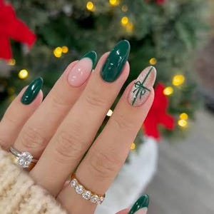 Puede incluir: Una mano con un anillo y varias uñas pintadas en una combinación de colores. Las uñas están pintadas en una combinación de verde, rosa y purpurina. Una uña tiene un diseño de lazo.