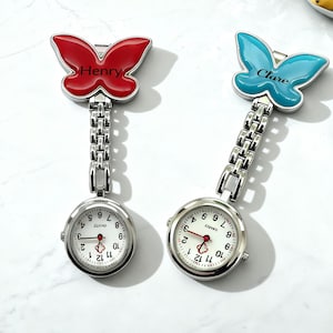 May include: Two silver nurse fob watches. One has a red butterfly top with the name "Henry", the other has a blue butterfly top with the name "Clare". Both watches have a white face with black numbers and a red second hand.