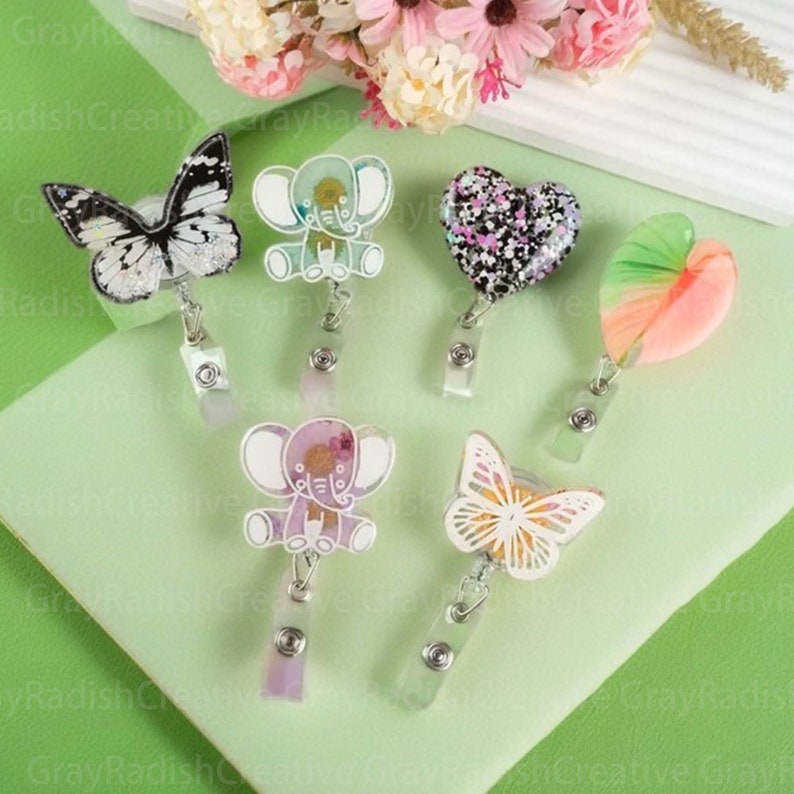 May include: Six colorful resin badge holders with different designs, including a butterfly, an elephant, a heart, and a leaf. The badge holders are attached to silver retractable badge reels.