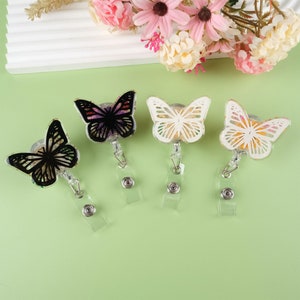 May include: Four butterfly-shaped retractable badge holders with clear plastic straps. The butterflies are black, white, and two different shades of yellow with dried flowers embedded in the resin.