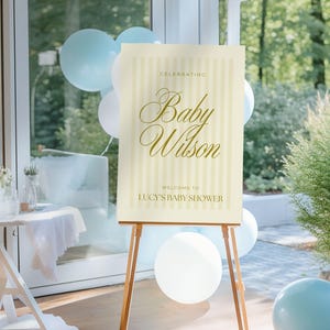 Large-format editable baby shower sign in yellow stripes, shown on a wooden easel surrounded by party decor — ideal for boy, girl, or gender-neutral showers.