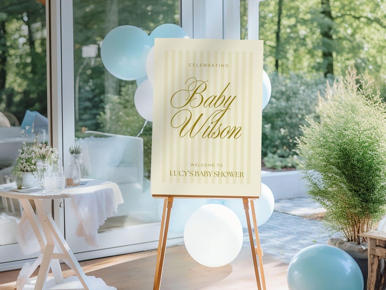 Large-format editable baby shower sign in yellow stripes, shown on a wooden easel surrounded by party decor — ideal for boy, girl, or gender-neutral showers.