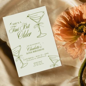 Könnte beinhalten: Eine Einladungskarte mit dem Text "She's a Tini Bit Older" in eleganter Schrift, mit Illustrationen von Martinigläsern. Die Karte ist für Charlottes 30. Geburtstag, mit Veranstaltungsdetails. Eine pfirsichfarbene Blume befindet sich im Hintergrund.