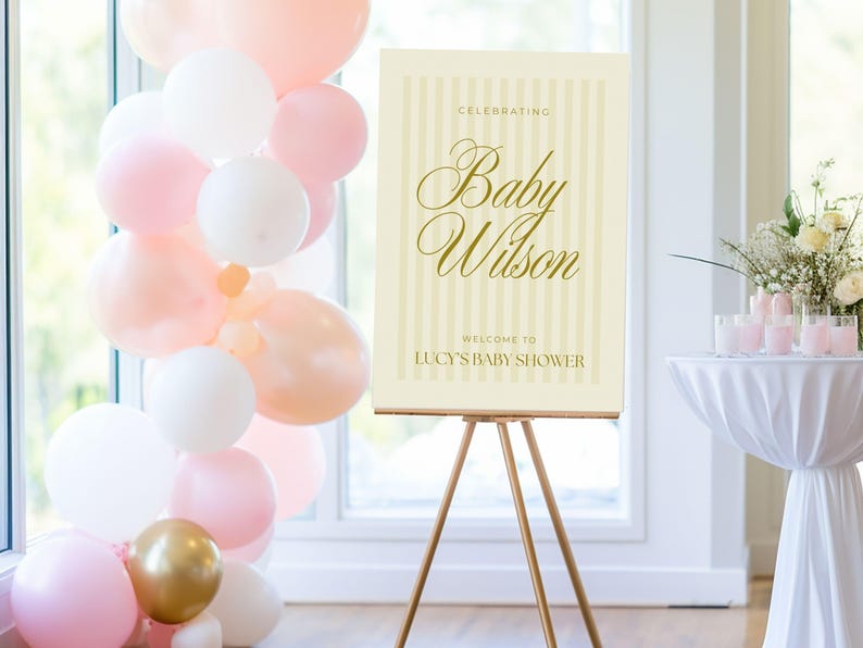 Gender-neutral yellow baby shower welcome sign displayed on a wooden easel at a styled shower setup with balloons and florals — editable A0 Canva template with soft vertical stripes.